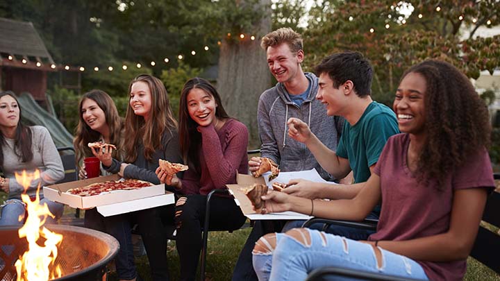 Teenagers around a bonfire eating pizza